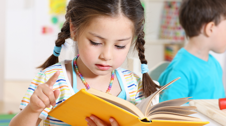 criança menina, com os cabelos de trança e um livro amarelo na mão, lendo representando o dia das crianças e o dia da leitura